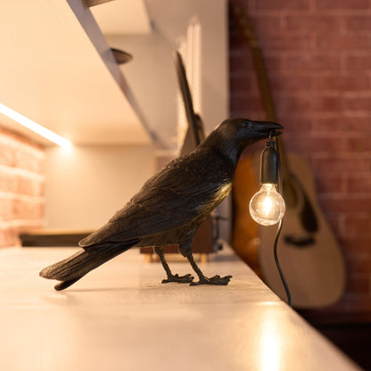 Stolní lampa s havranem držícím žárovku